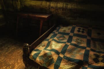 photo of antique bed with quilt on top and bench at foot of bed