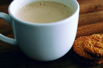 photo of latte on a wooden table next to two cookies