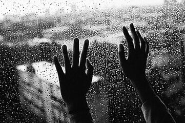 black and white photo of hands pressed up against the inside of a rainy window